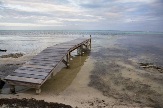 A short wooden pier on the beach at sunset.