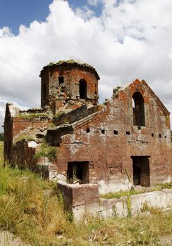 Portrait of Kizil Kilsie with tall grass, Red Church ruins of dilapidated and derelict Church Cappadocia Turkey dating to the 6th century, rustic colors, red limestone, tall grass crop area and copy space