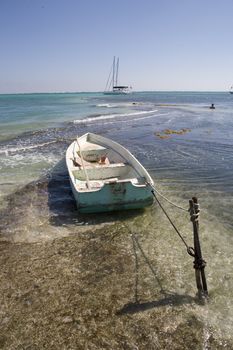 A small wooden rowboat is tied in the shallows close to a beautiful beach in the Gulf of Mexico.