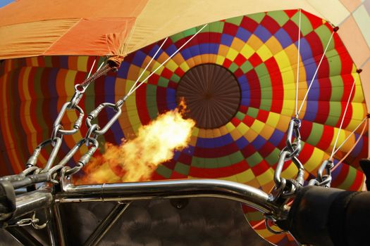 Close-up of hot air balloon rigging and flames from jets, multi colored balloon, guide ropes, landscape, tight crop