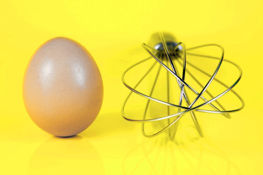 An egg and and a egg beater together isolated against a yellow background