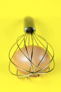 An egg and and a egg beater together isolated against a yellow background