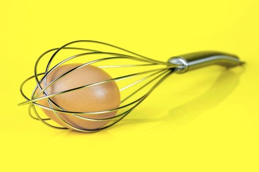 An egg and and a egg beater together isolated against a yellow background