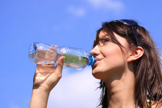 Girl drinking water against blue sky in sunny day