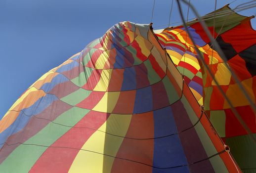 Landscape of deflating hot air balloon, multi colored, blue sky, guy ropes, guide ropes, crop space and copy space