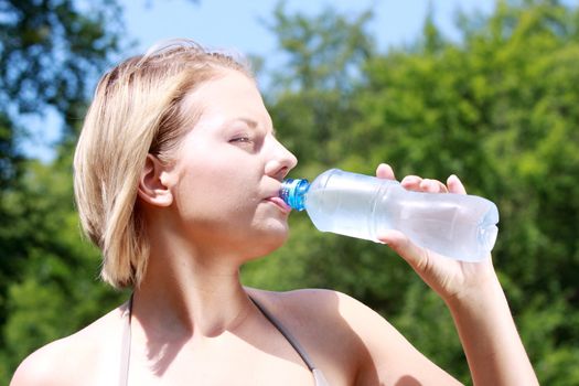 Pretty woman drinking water on the summer glade