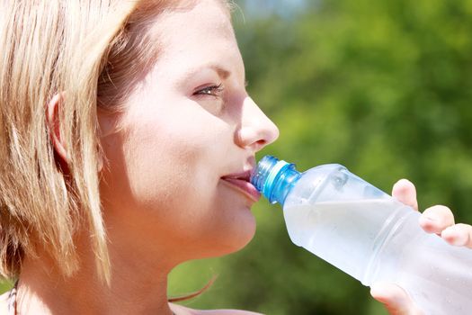 Pretty woman drinking water on the summer glade