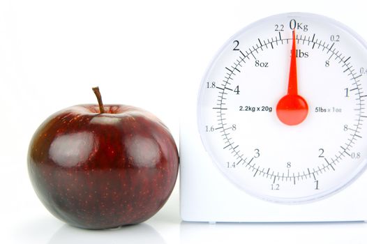 A red apple on top of a set of kitchen scales isolated against a white background