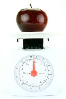 A red apple on top of a set of kitchen scales isolated against a white background
