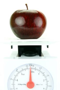 A red apple on top of a set of kitchen scales isolated against a white background