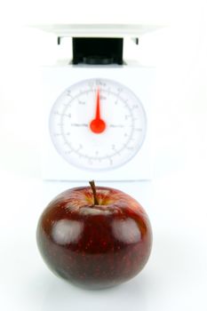 A red apple on top of a set of kitchen scales isolated against a white background