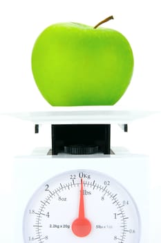 A green apple on top of a set of kitchen scales isolated against a white background
