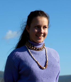 Beautiful girl in a necklace laughs at the blue sky