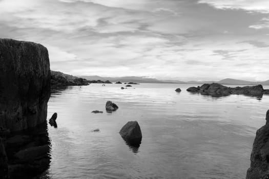 black and white scenic view in kerry ireland of rocks and sea with mountains against a beautiful blue cloudy sky