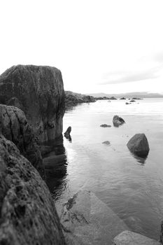 black and white scenic view in kerry ireland of rocks and sea with mountains against a beautiful blue cloudy sky