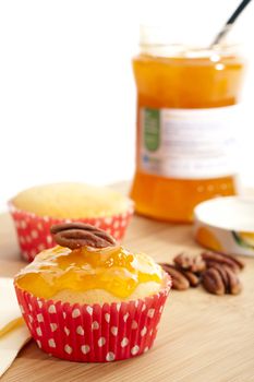 Yellow cupcake topped with jam and a pecan, with jar in background