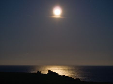 Full bright moon over the sea ocean with far away lights in the background