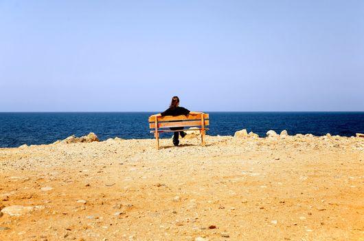 The woman sits on a bench at coast