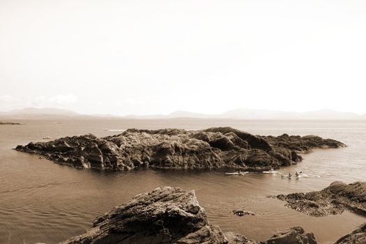 kayaks in a scenic view in kerry ireland of rocks islands and sea with mountains against a beautiful blue cloudy sky