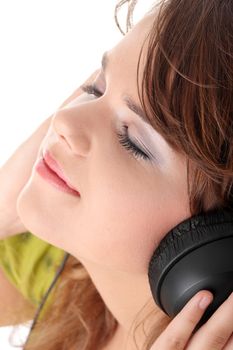 Beautiful teenage girl in a green dress listening to music with big headphones, isolated on white