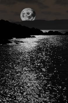 scenic view in kerry ireland of rocks and sea with a moon rising behind mountains against a night sky