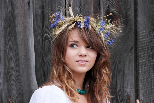 Beautiful young girl with grain wreath against old wood wall