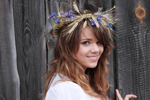 Beautiful young girl with grain wreath against old wood wall