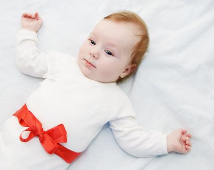 Adorable baby boy in light with red ribbon as gift
