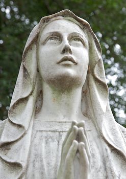 Ancient cemetary heastone of a woman in prayer looking toward heaven.  Spider webs cover the eyes giving the image a spooky and creepy feeling.