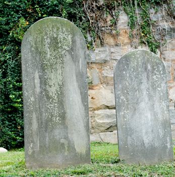 Two ancient headstones in a cemetery.  The aging of the stone has worn away any words that may have once been present.