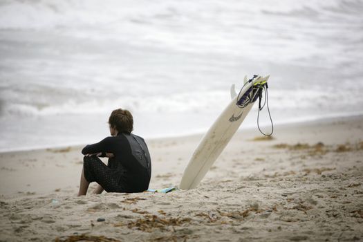 young surfer sitting on the beach and watching the waves