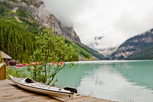 A canoe on the deck of the beautiful turquoise colored Lake Louis against the backdrop of the foggy majestic mountains of the Canadian Rockies