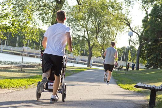 A man jogging while pushing a stroller on a beautiful sunny afternoon along side Wascana lake