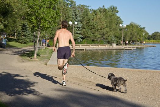 A man jogging along Wascana lake with his dog on a leash following behind