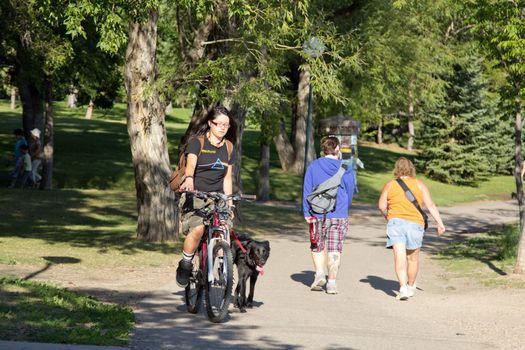 A young woman waling her dog on her bike and listening to her music