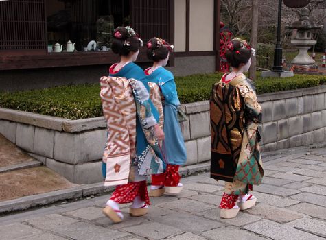  Three geishas walking in a traditional Kyoto street.There is some intended motion blur due to the stepping attitude.         