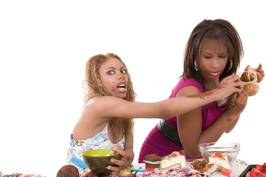 Two black girls fighting over a bunch of muffins while the entire table in front of them is loaded with food