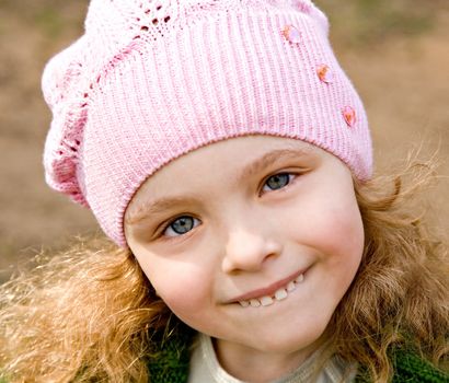 Portrait of the cheerful little girl in a pink cap with long hair
