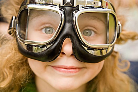 The ridiculous little girl with long hair and grey eyes in motorcycle glasses close up
