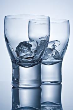Two empty glasses with ice pieces on a reflecting surface
