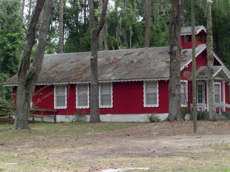 A red farm house is nestled in between tall trees and the forest