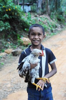 Neluwa, Sri Lanka - January 27, 2011: Sri Lankan boy from small sri lankan village carrying  chicken in his hands and looking to the camera