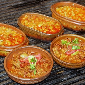 Serbian special meal "Leskovacka Muckalica" in Clay dish with "tavce na gravce" behind, shallow DOF