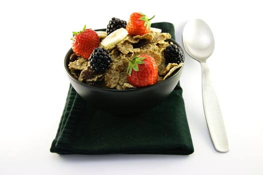 Crunchy looking delicious bran flakes and juicy fruit in a black bowl with a spoon on a black napkin on a white background