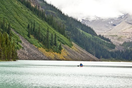 People paddling in a canoe on the beautiful turquoise colored Lake Louis against the backdrop of the majestic mountains of the Canadian Rockies partially covered with fog