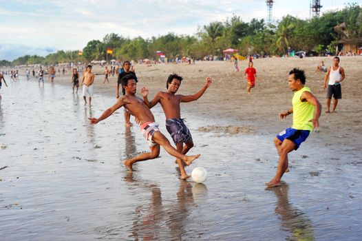 Bali, Indonesia - April 4, 2011: People plaing soccer on the  Kuta beach.Kuta's six-kilometer-long, crescent-shaped surfing beach, protected by a coral reef at its southern end, and long and wide enough for Frisbee contests and soccer games, is famous for its beautiful tropical sunsets.
