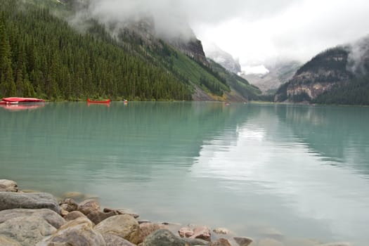 The beautiful turquoise colored Lake Louis against the backdrop of the majestic mountains of the Canadian Rockies partially covered with fog