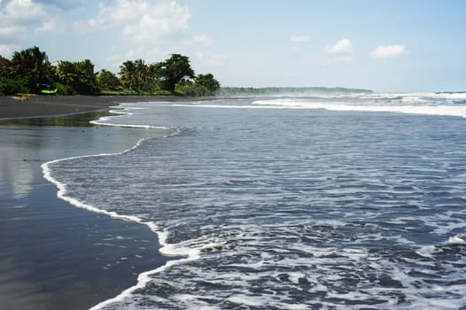 Tide coming in from the sea on black sand beach. Bali, Indonesia