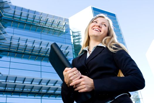 Blonde business woman posing in front of a modern blue office building