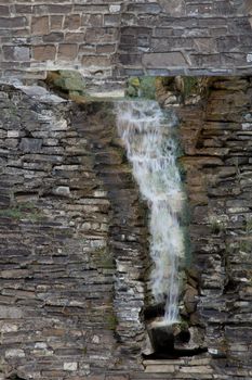 A tiny waterfall flowing down on a very old stone wall